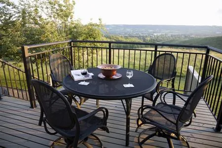 A black metal railing surrounds a wooden deck with a table and chairs overlooking a scenic valley.