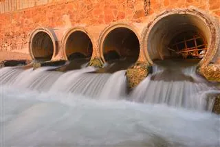 Water flowing from four large concrete drainage pipes set into a stone wall.