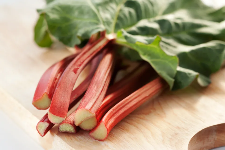 A bundle of red rhubarb stalks with green leaves lying on a wooden cutting board.