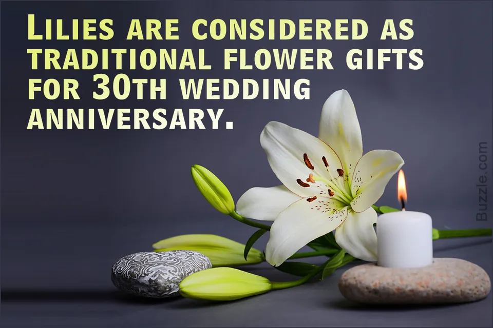 A white lily flower with green buds rests beside a lit candle and stones on a dark surface.