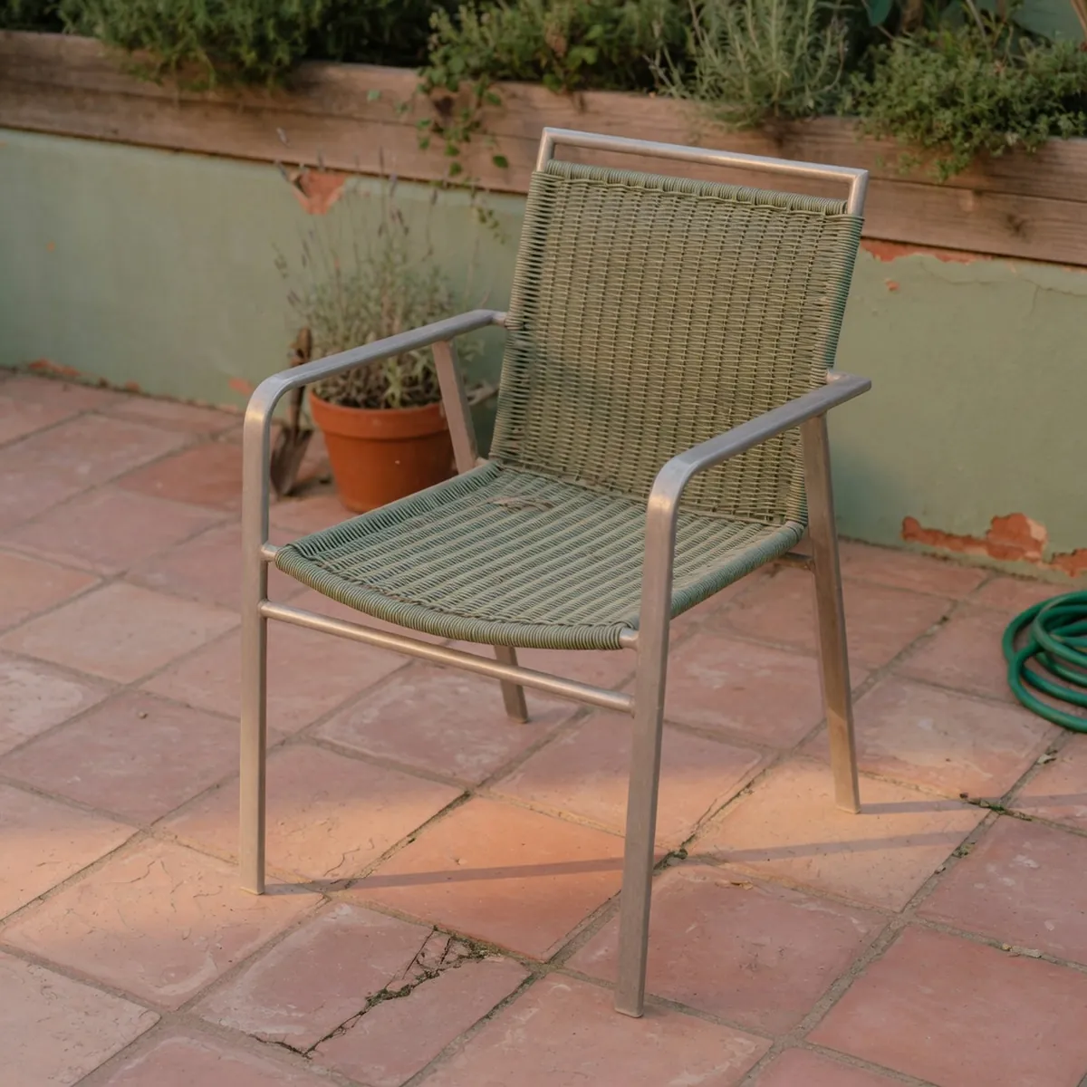A sleek aluminum patio chair with woven seat and backrest on a paved terrace.