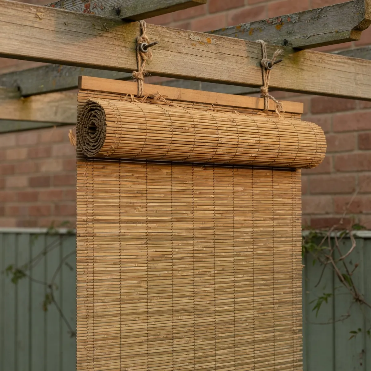 Woven bamboo roll-up blinds hanging vertically from a wooden pergola beam.