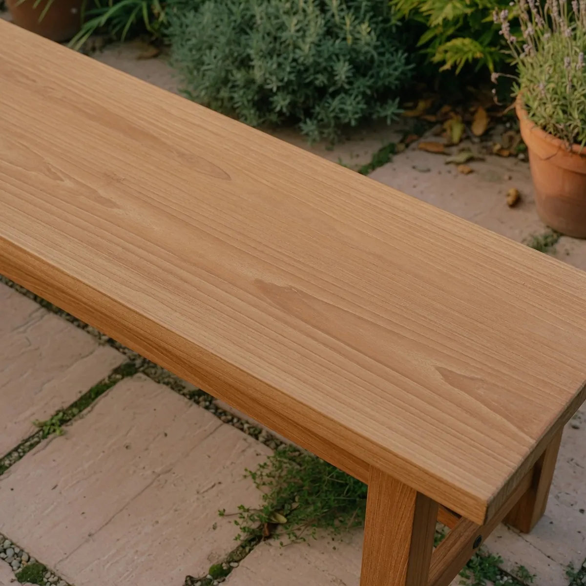A close-up of a smooth, honey-brown teak wood bench surface showing its straight grain pattern.